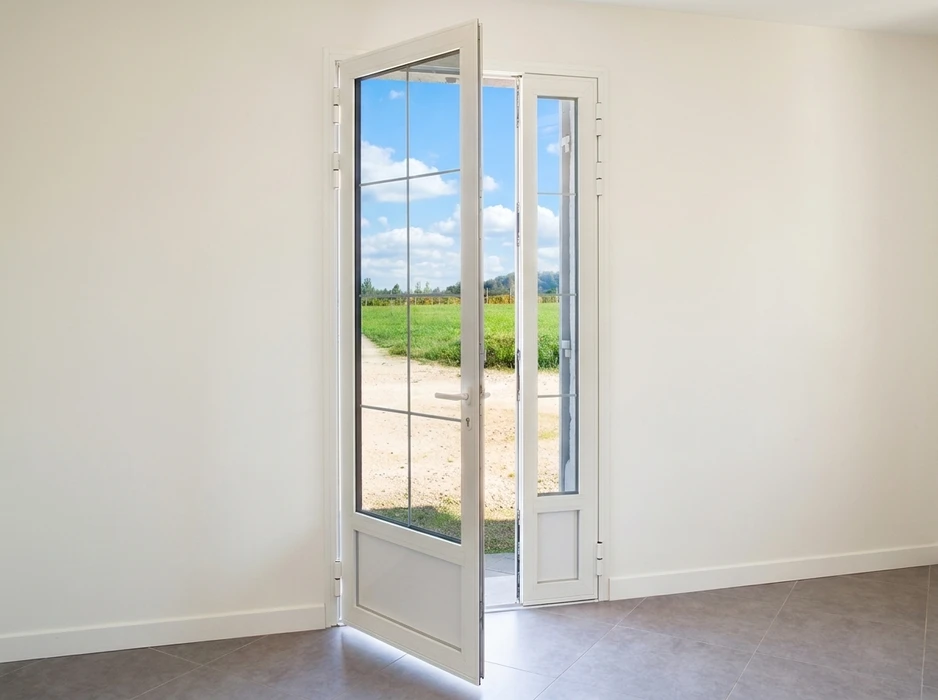 Intérieur lumineux avec porte-fenêtre blanche à deux vantaux en PVC, vitrée avec petits-bois intégrés, donnant sur un paysage rural verdoyant