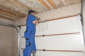Technicien en combinaison bleue installant une porte de garage sectionnelle dans un garage résidentiel