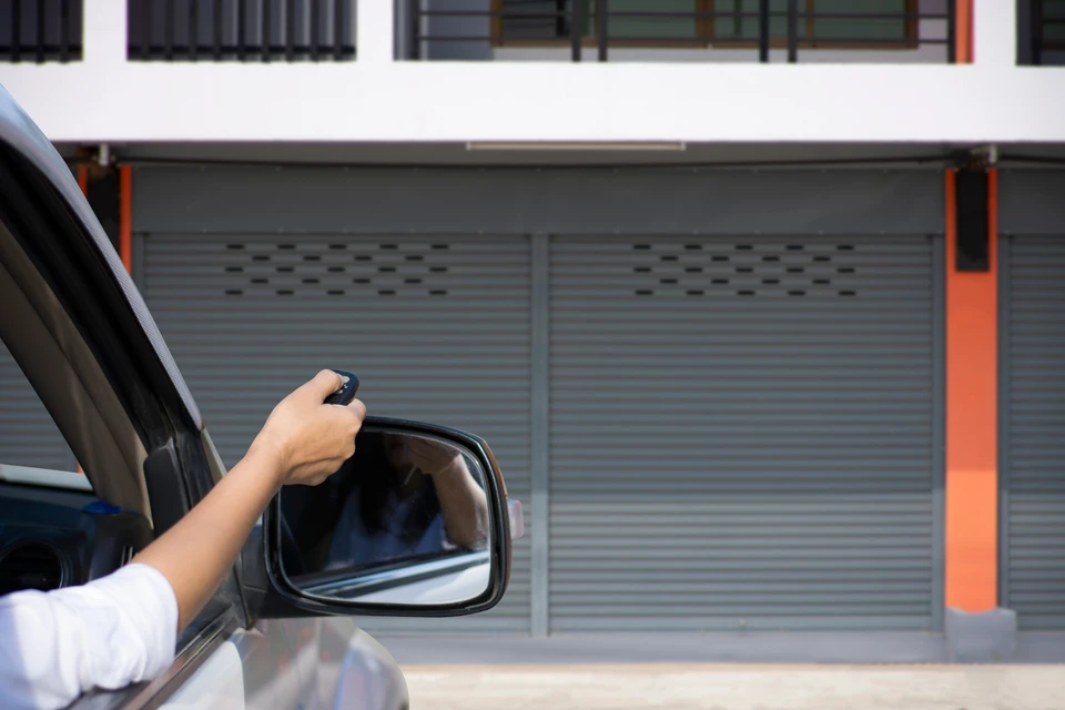 Personne en voiture utilisant une télécommande depuis la fenêtre conducteur pour ouvrir un portail de garage ou d'entrepôt industriel