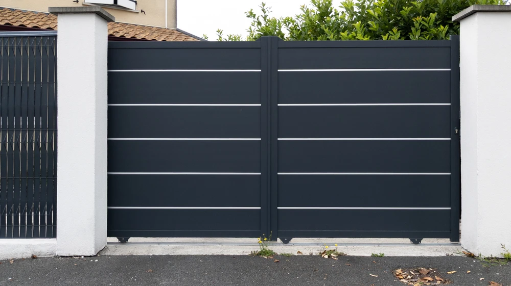 Portail coulissant en aluminium anthracite avec lames horizontales et inserts blancs, installé entre piliers en béton blanc