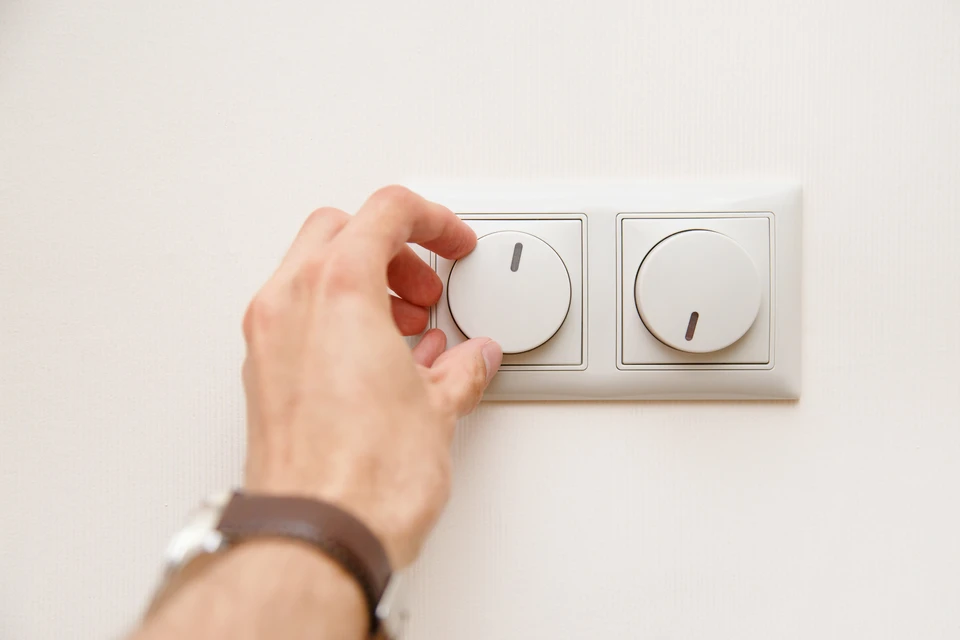 Une main ajuste un variateur électrique rotatif blanc monté sur mur