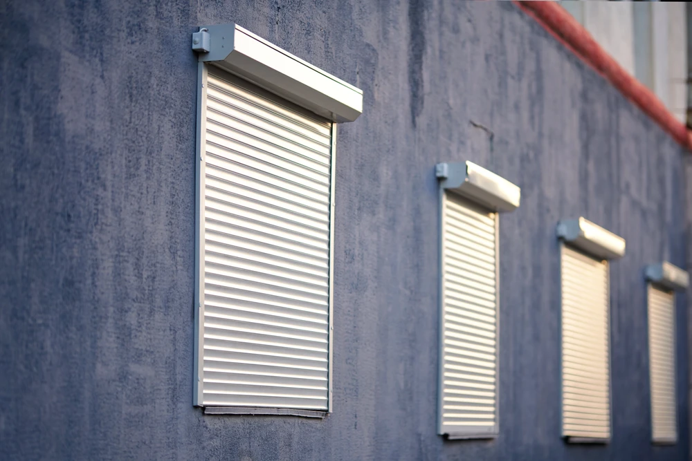 Façade extérieure de bâtiment avec volets roulants blancs installés sur mur texturé bleu-gris