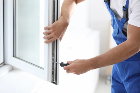 Un technicien en salopette bleue installe ou ajuste une fenêtre à double vitrage dans un intérieur résidentiel moderne